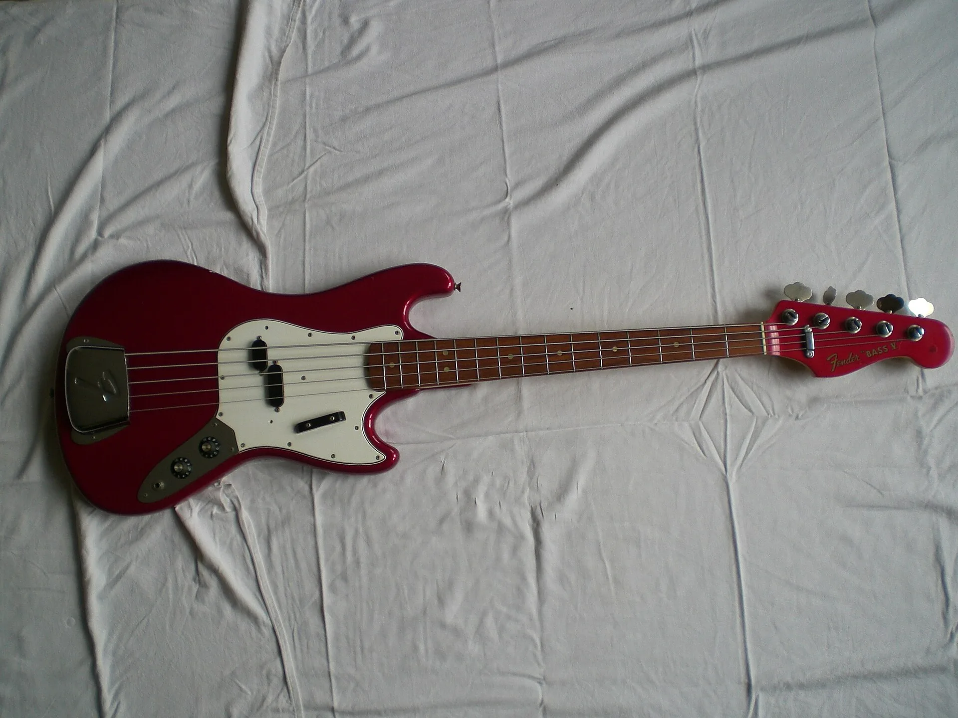 1965 Fender Bass V in red with matching headstock, lying on a white sheet