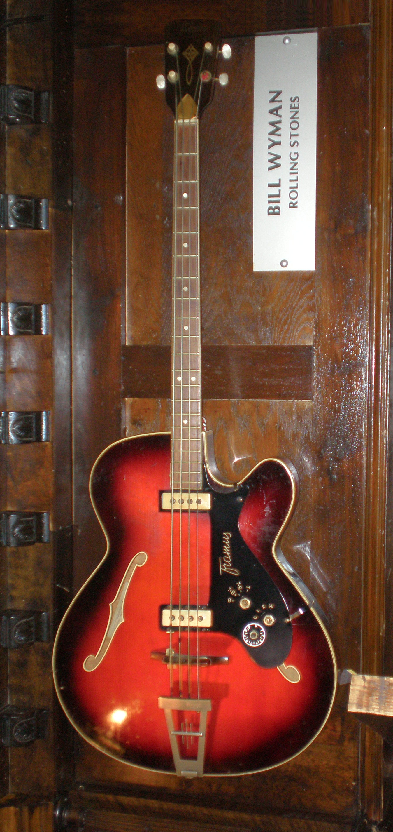 Red-burst Framus Star Bass hollow-body bass hanging in a display case under a Bill Wyman, Rolling Stones label