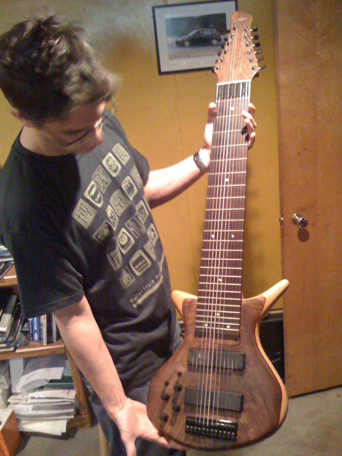 A man holds up a wooden-bodied Warr touch guitar with a wide many-string fretboard, two long pickups and a row of tuners down the headstock